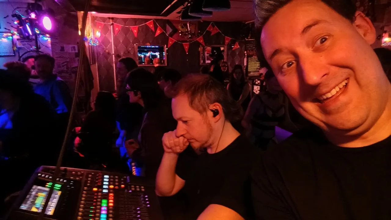 Dan is concentrating on an X32 mixer in a small, dark venue while his more energetic friend is mugging into camera.
